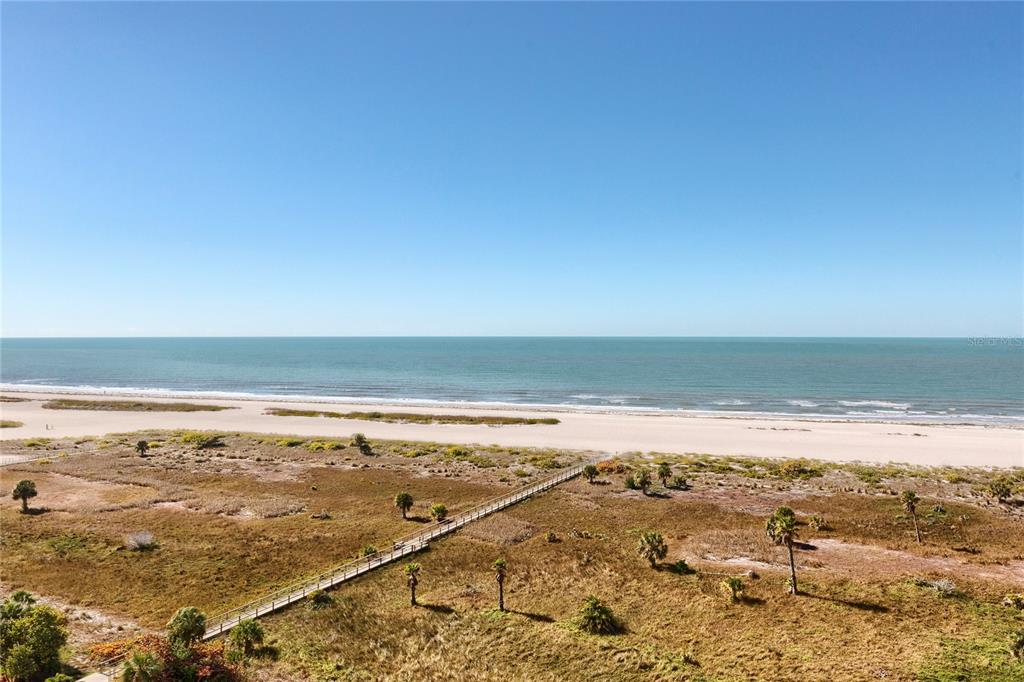 An elevated view of a sandy beach, ocean, and a wooden boardwalk through coastal vegetation — 1200 GULF BOULEVARD UNIT 1002, CLEARWATER, FL