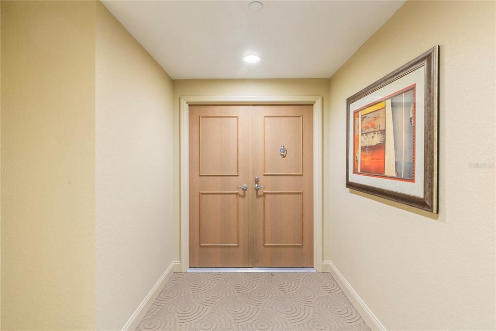 A small entryway features double wooden doors, beige walls, and patterned carpet flooring — 1200 GULF BOULEVARD UNIT 1002, CLEARWATER, FL