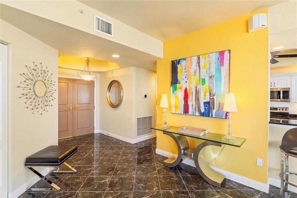 An entryway with dark marble tile flooring, a yellow accent wall, and a glass console table — 1200 GULF BOULEVARD UNIT 1002, CLEARWATER, FL
