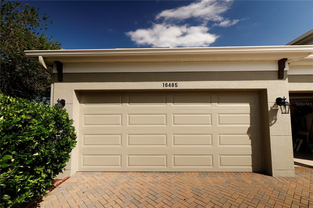 A beige garage door with rectangular panels is set into a stucco exterior wall — 16485 COURTYARD LOOP, LAND O LAKES, FL