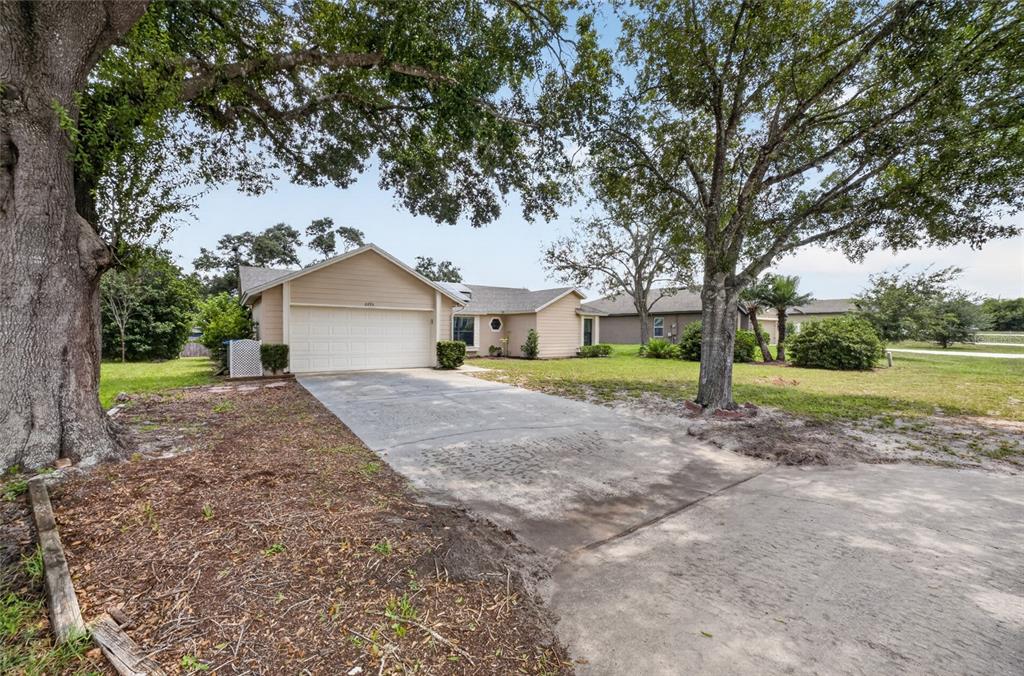 A tan single-story house with a two-car garage and a concrete driveway under large trees — 2495 E TIPTON DRIVE, DELTONA, FL