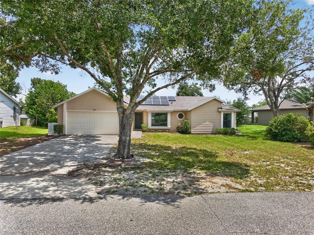 A single-story house with a beige exterior, a two-car garage, and solar panels on the roof — 2495 E TIPTON DRIVE, DELTONA, FL