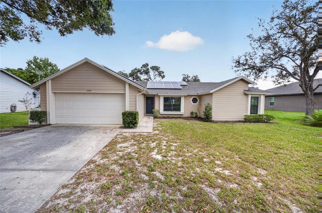 A single-story house with tan siding, a two-car garage, and solar panels on the roof — 2495 E TIPTON DRIVE, DELTONA, FL