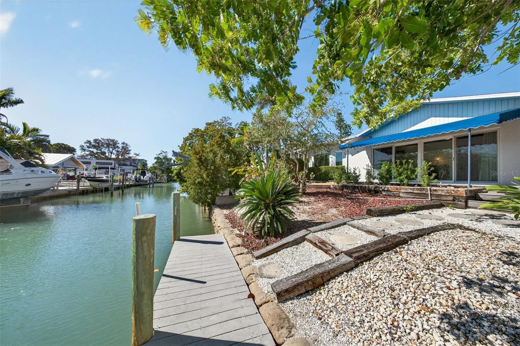 A wooden dock extends into a canal beside a house with a blue awning — 550 DE NARVAEZ DRIVE, LONGBOAT KEY, FL