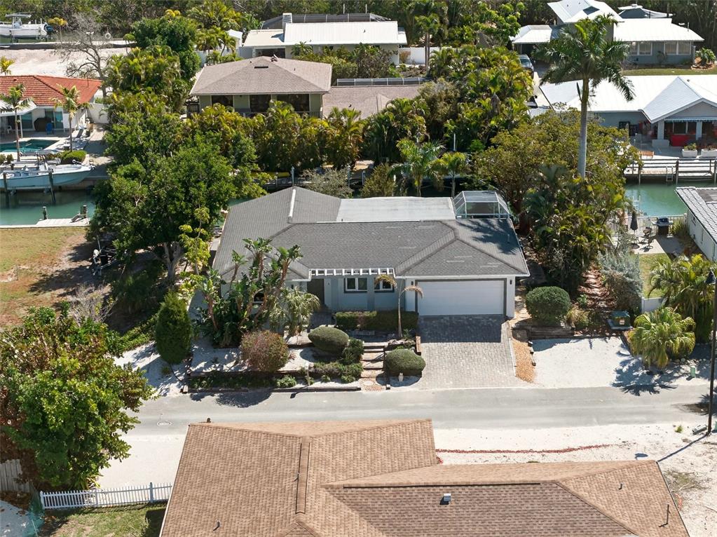An aerial view shows a single-story house with a gray roof, garage, and waterfront access — 550 DE NARVAEZ DRIVE, LONGBOAT KEY, FL