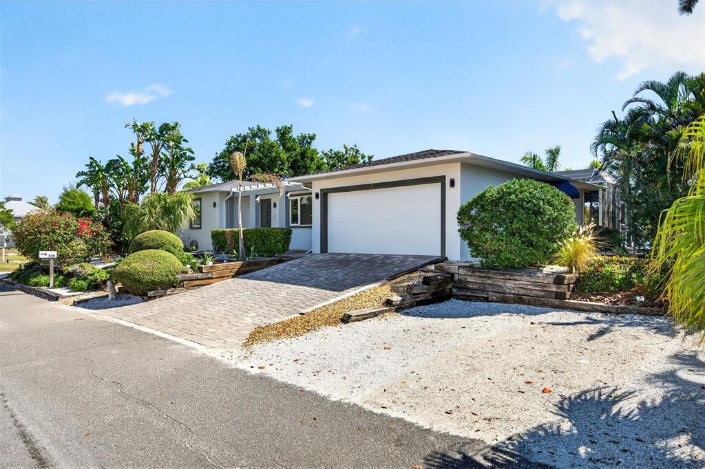 A single-story house features a paved driveway, a white garage door, and landscaped front yard — 550 DE NARVAEZ DRIVE, LONGBOAT KEY, FL