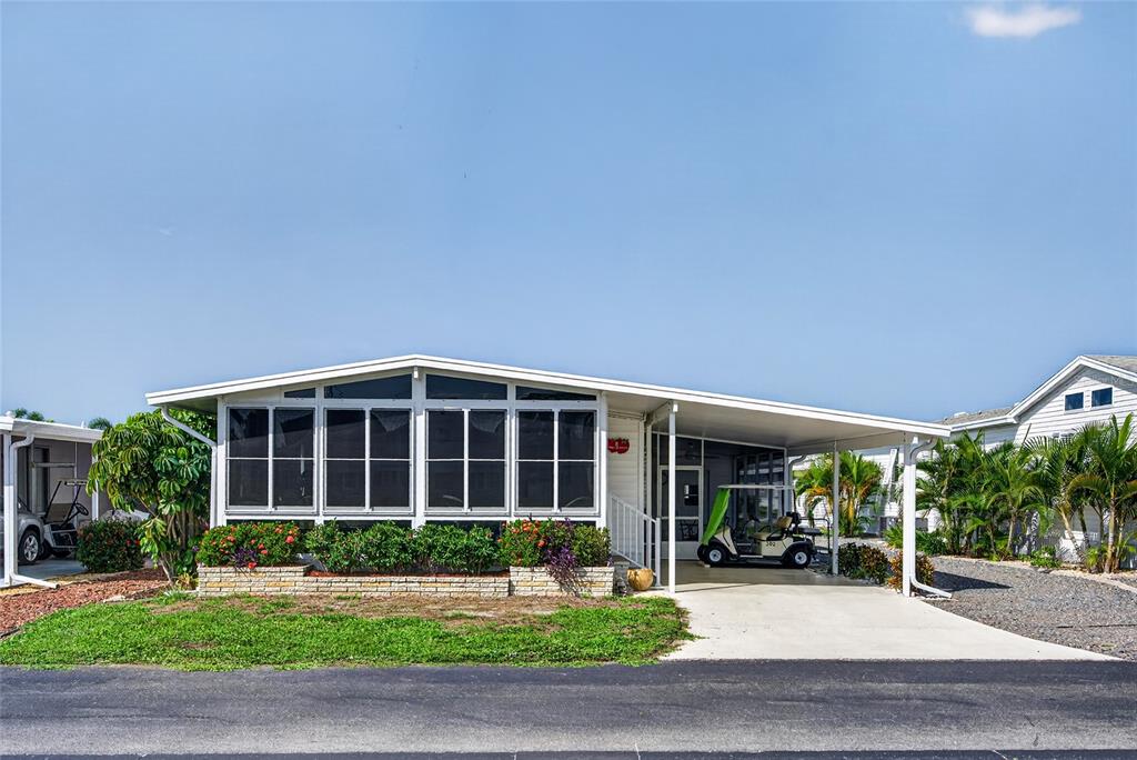 A single-story manufactured home features a screened-in porch, a carport, and a landscaped front yard — 11 DEL PRADO DRIVE, ENGLEWOOD, FL