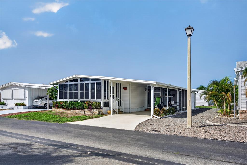A white manufactured home with a screened-in porch and a concrete driveway under a blue sky — 11 DEL PRADO DRIVE, ENGLEWOOD, FL