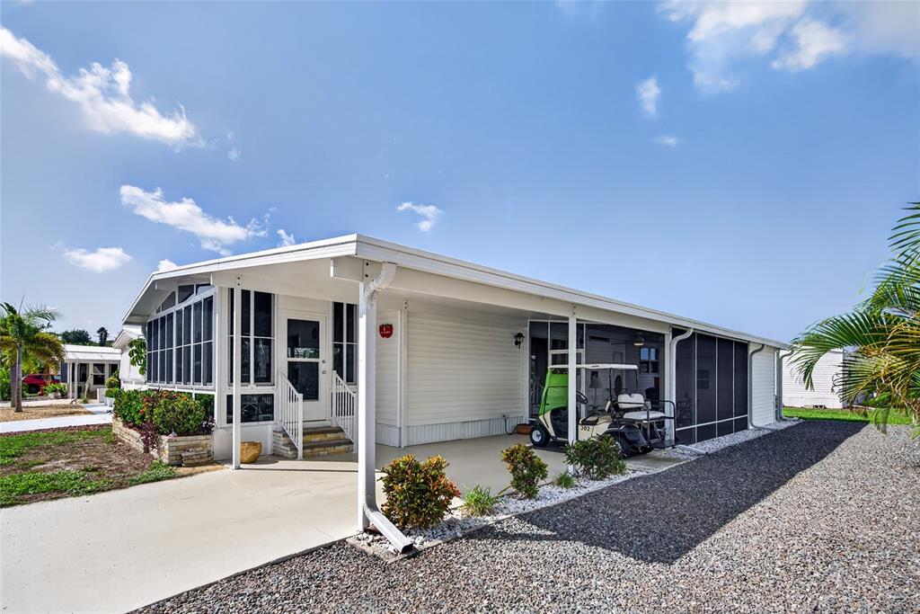 A white mobile home features a screened-in porch, a carport with a golf cart, and gravel — 11 DEL PRADO DRIVE, ENGLEWOOD, FL