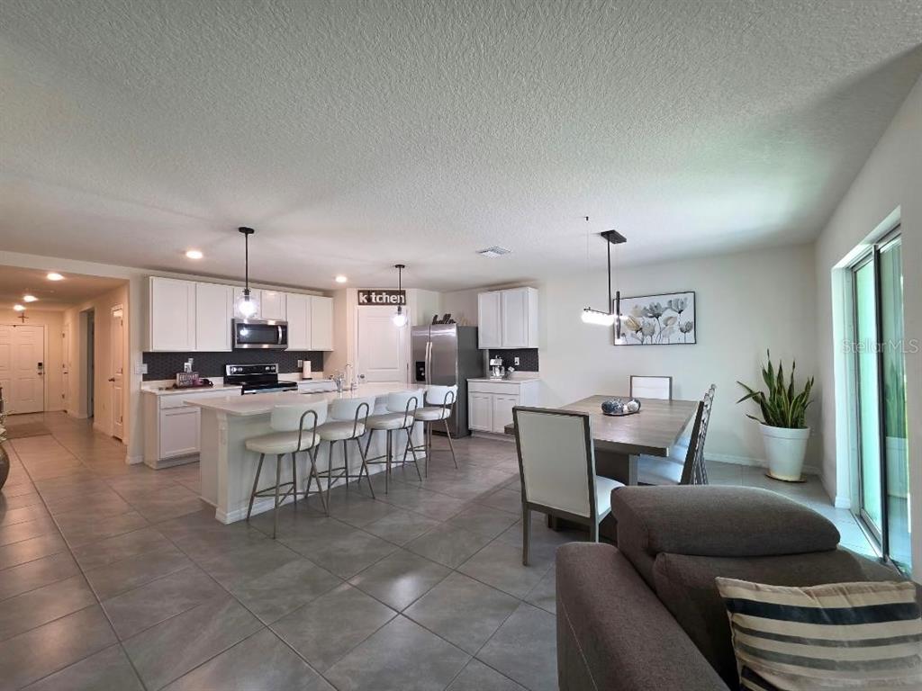 An open-concept kitchen and dining area features white cabinetry, a central island, and tile flooring — 4446 BAYRIDGE COURT, SPRING HILL, FL