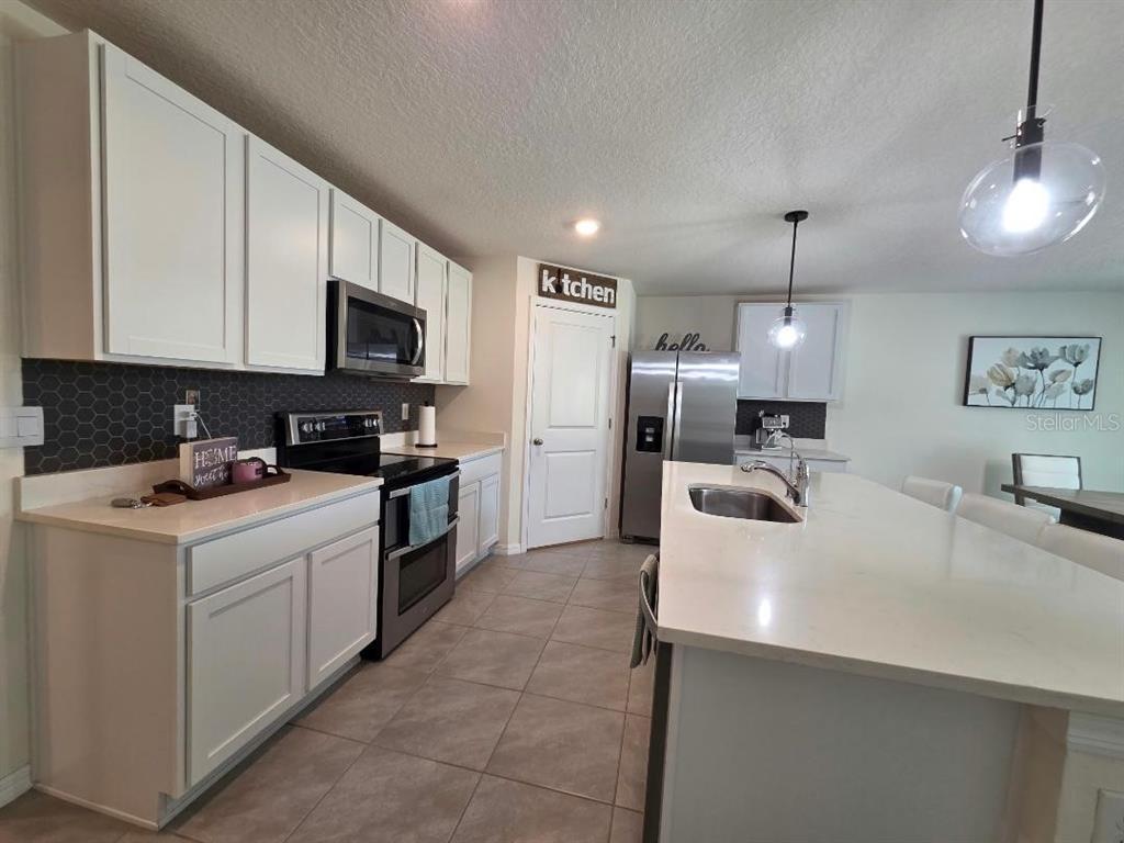 A kitchen features white cabinets, a large island with a sink, and dark tiled backsplash — 4446 BAYRIDGE COURT, SPRING HILL, FL
