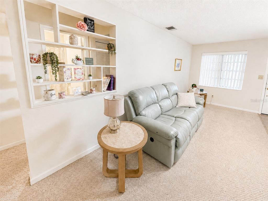 A living room features a light blue reclining sofa, a round side table, and built-in shelving — 1131 ORANGE TREE CIRCLE W UNIT C, PALM HARBOR, FL