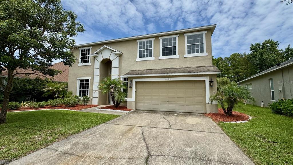 A two-story house with a beige stucco exterior, a two-car garage, and a concrete driveway — 14125 DEEP LAKE DRIVE, ORLANDO, FL
