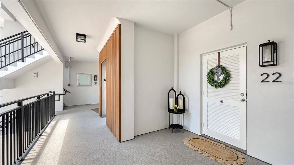 An outdoor apartment hallway features a white door labeled 22, a small table, and stairs — 174 GOLDEN GATE POINT UNIT 22, SARASOTA, FL