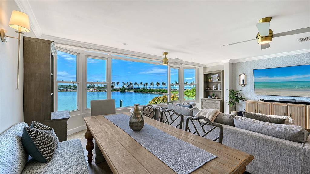 A dining and living area features a wooden table, gray sofa, and large waterfront windows — 174 GOLDEN GATE POINT UNIT 22, SARASOTA, FL