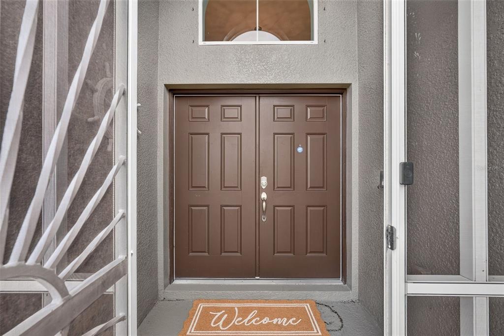 A brown double front door with a welcome mat sits inside a screened-in entryway — 319 19TH STREET NW, RUSKIN, FL