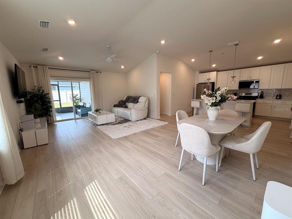 An open-concept living and dining area features light wood flooring, white furniture, and a kitchen — 354 BOULDER LANE, ST JOHNS, FL