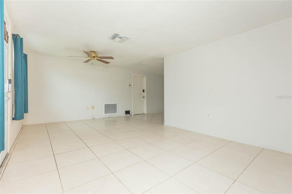 An empty room features white walls, light-colored tile flooring, a ceiling fan, and blue curtains — 1447 WEYFORD LANE, HOLIDAY, FL