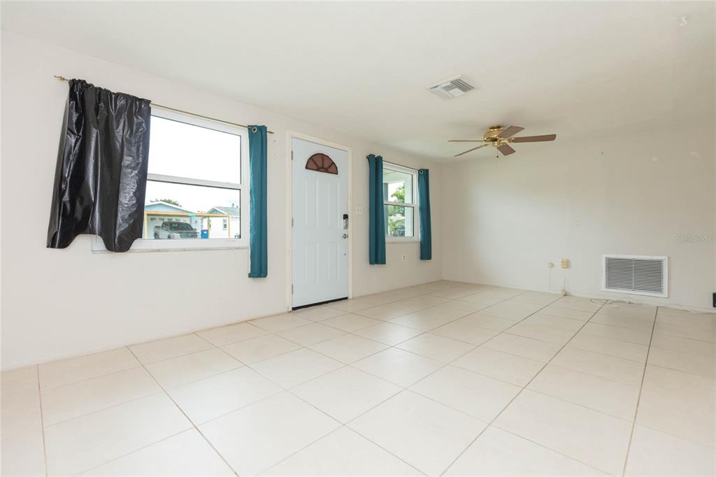 A living room features white tile flooring, a ceiling fan, and a white entry door — 1447 WEYFORD LANE, HOLIDAY, FL