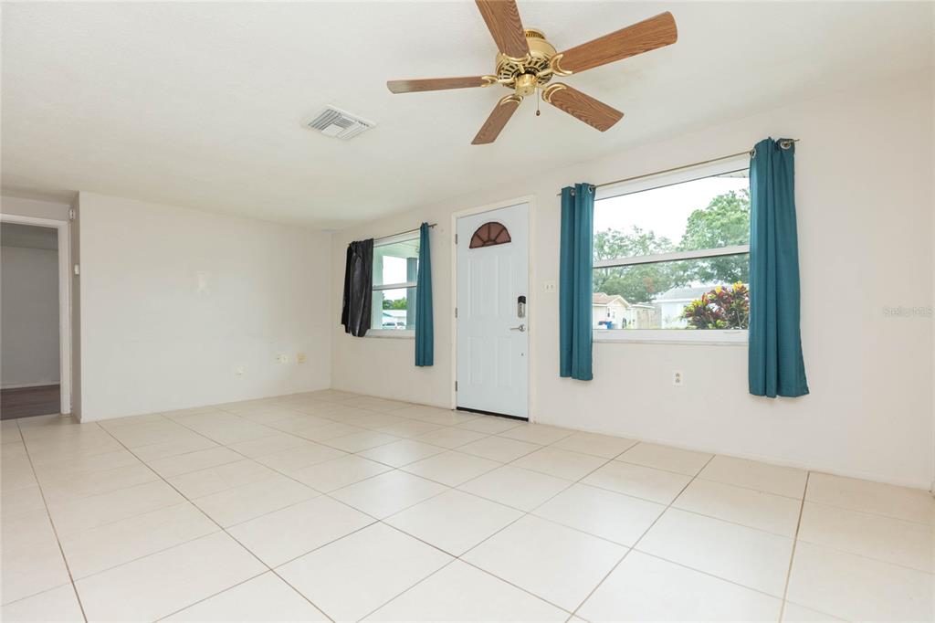 A living room with white tiled floors, a ceiling fan, and a white front door — 1447 WEYFORD LANE, HOLIDAY, FL
