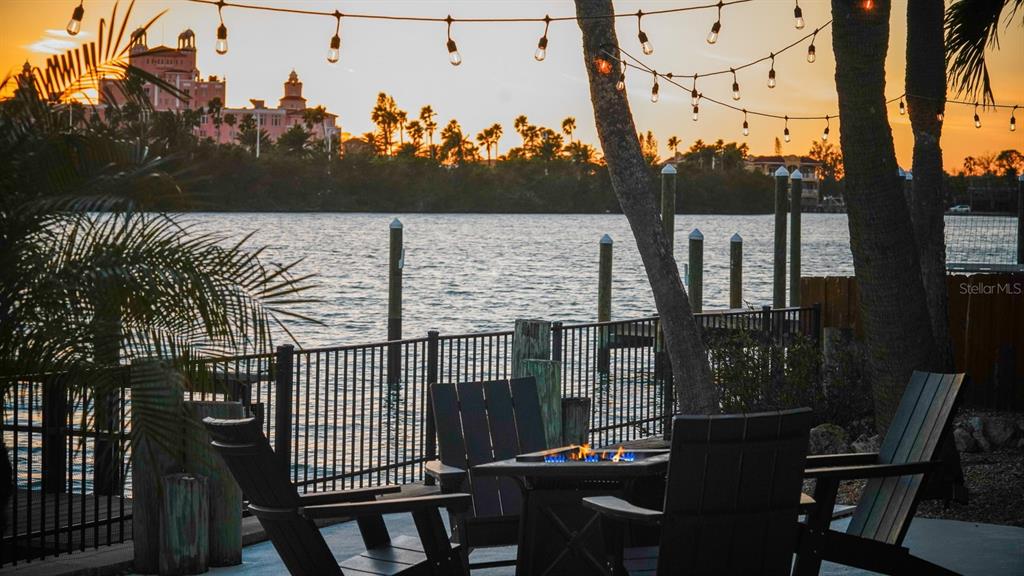 A patio with a fire pit and chairs overlooks a body of water at sunset — 3606 BELLE VISTA DRIVE E, ST PETE BEACH, FL