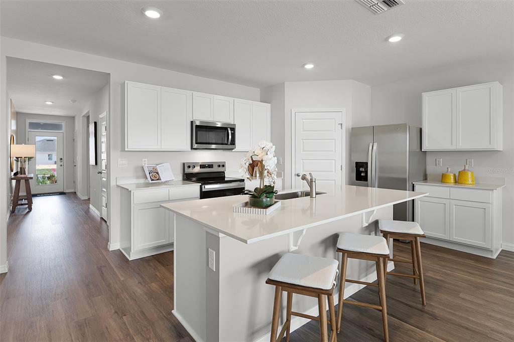 A modern kitchen features white cabinets, stainless steel appliances, a quartz island, and wood flooring — 2490 AVEENO AVENUE, HAINES CITY, FL