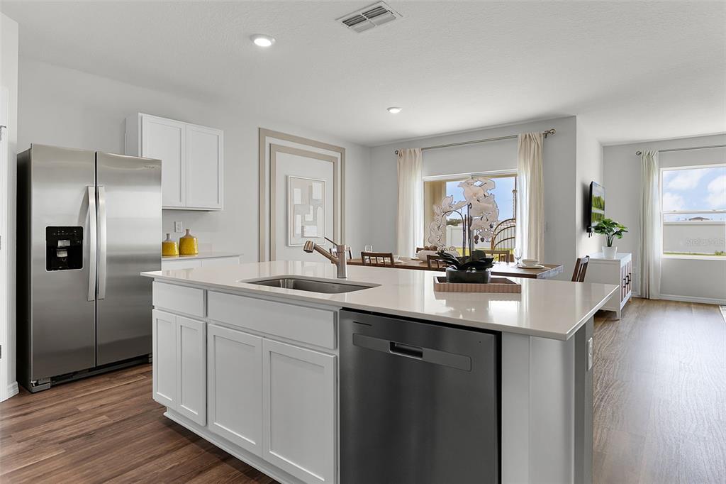A modern kitchen features a white island with a sink, stainless appliances, and wood flooring — 2490 AVEENO AVENUE, HAINES CITY, FL