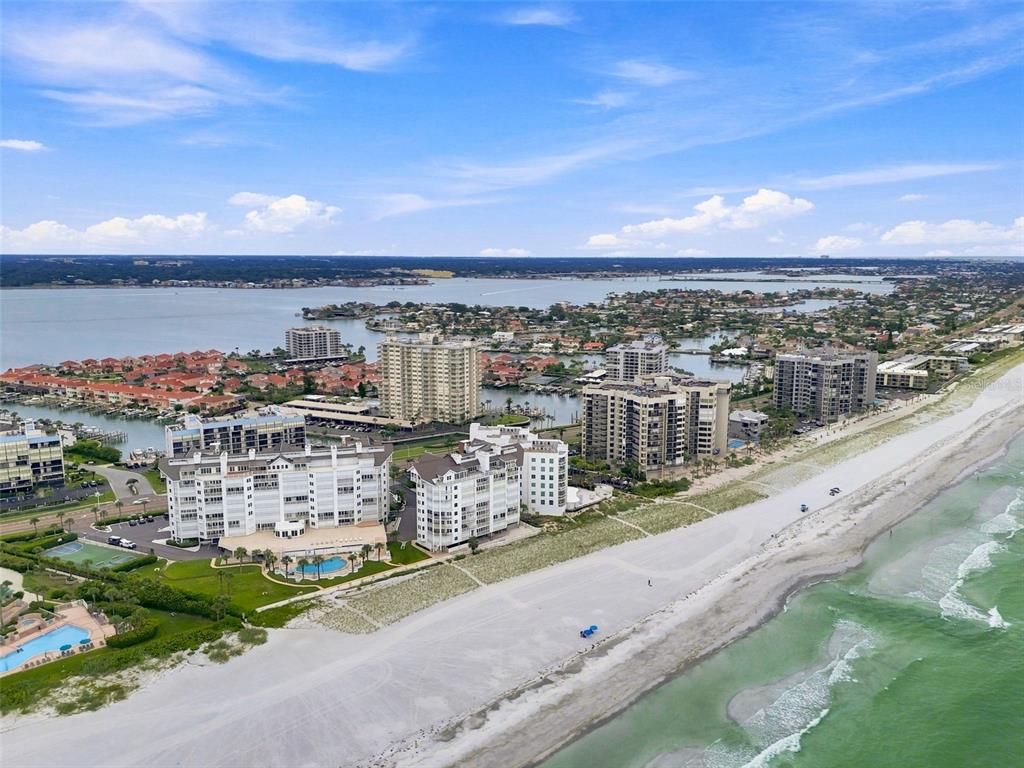 An aerial view shows beachfront condominiums, a swimming pool, and a large bay with houses — 1586 GULF BOULEVARD UNIT 2103, CLEARWATER, FL