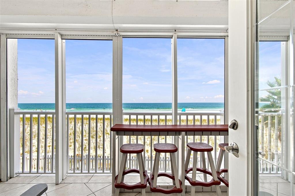 A screened-in balcony features a high-top table with three stools overlooking a sandy beach — 1586 GULF BOULEVARD UNIT 2103, CLEARWATER, FL