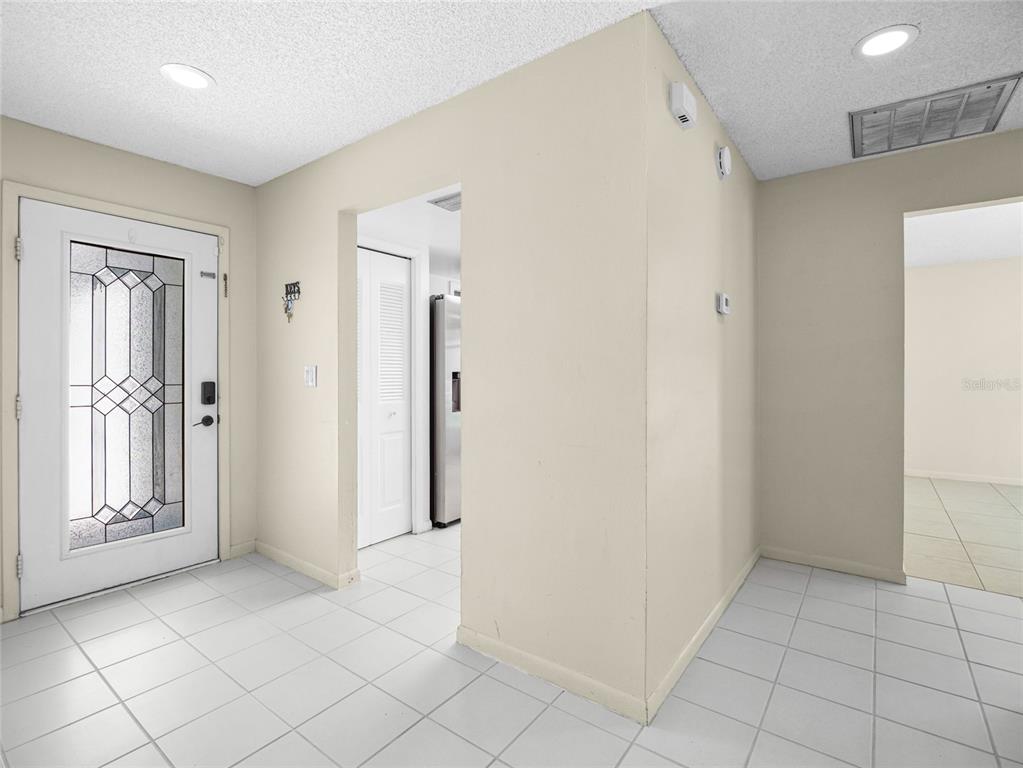 An entryway with white tiled floors, a glass-paneled front door, and beige walls — 1644 PARAKEET COURT, MELBOURNE, FL