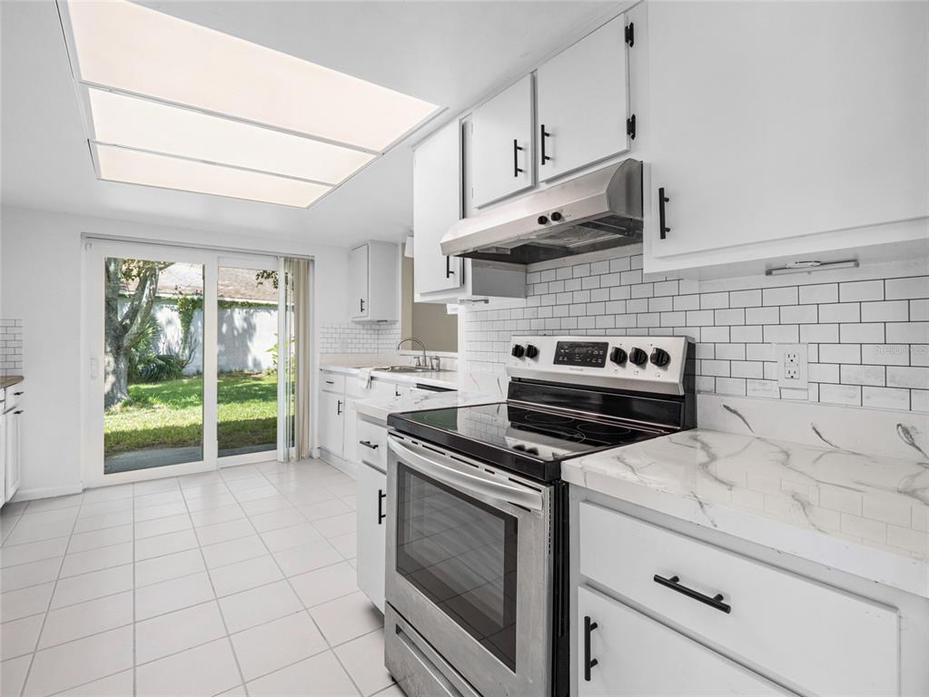 A kitchen features white cabinets, marble-look countertops, a stainless steel stove, and a sliding door — 1644 PARAKEET COURT, MELBOURNE, FL