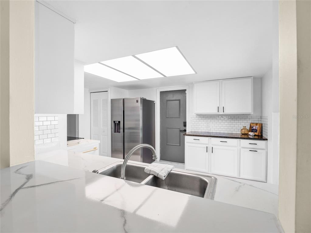 A kitchen features white cabinets, a stainless steel refrigerator, a double sink, and subway tile — 1644 PARAKEET COURT, MELBOURNE, FL