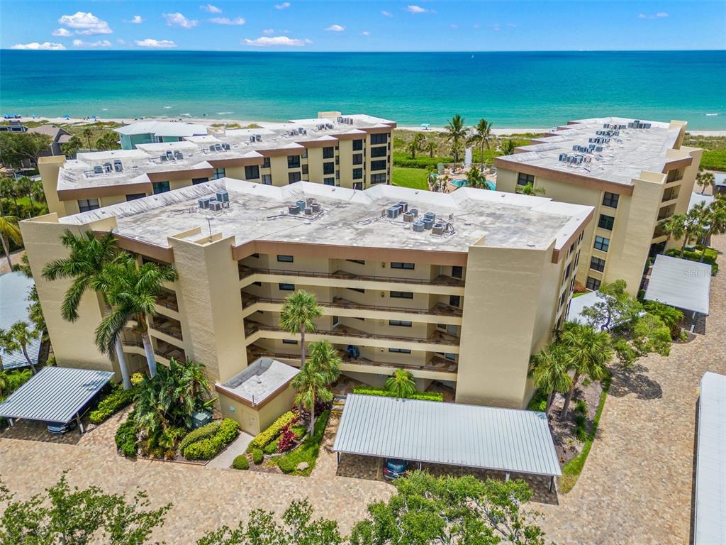 An aerial view shows a multi-story tan apartment building with a flat roof near the ocean — 8770 MIDNIGHT PASS ROAD UNIT 302B, SARASOTA, FL