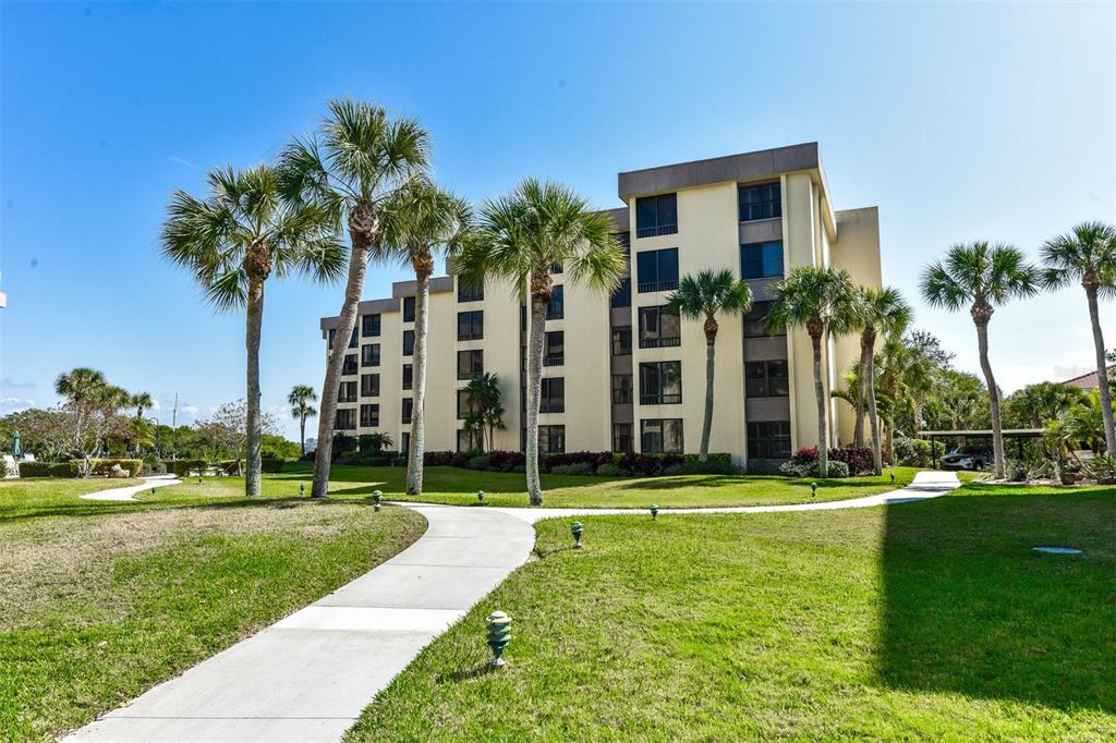 A multi-story apartment building with a concrete walkway surrounded by palm trees and grass — 8770 MIDNIGHT PASS ROAD UNIT 302B, SARASOTA, FL