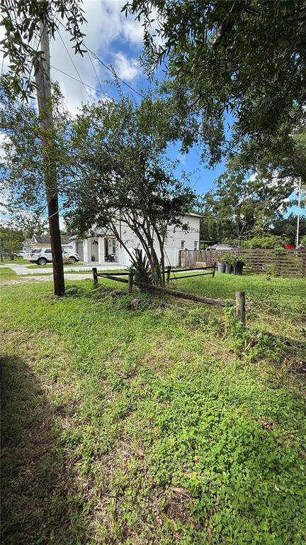 A grassy yard features a wooden fence, a small tree, and a house in the background — 8602 N ROME AVENUE, TAMPA, FL