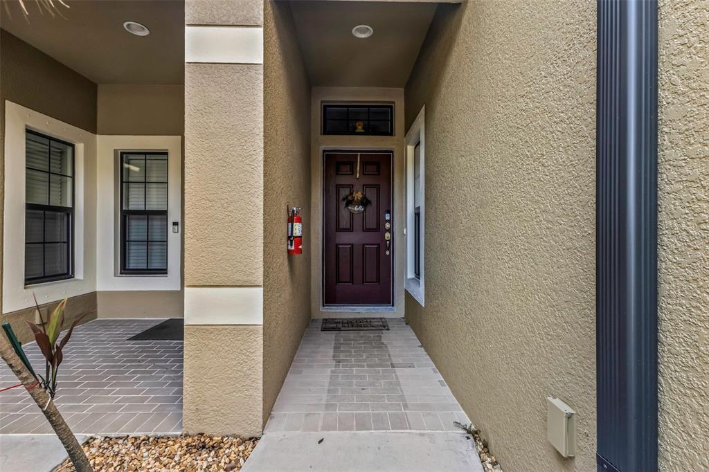 The exterior entrance features a dark red front door, a fire extinguisher, and tiled flooring — 7826 52ND TERRACE E, BRADENTON, FL