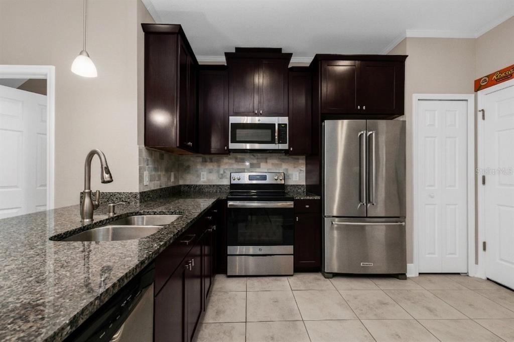 A kitchen features dark wood cabinets, granite countertops, stainless steel appliances, and light tile flooring — 7826 52ND TERRACE E, BRADENTON, FL
