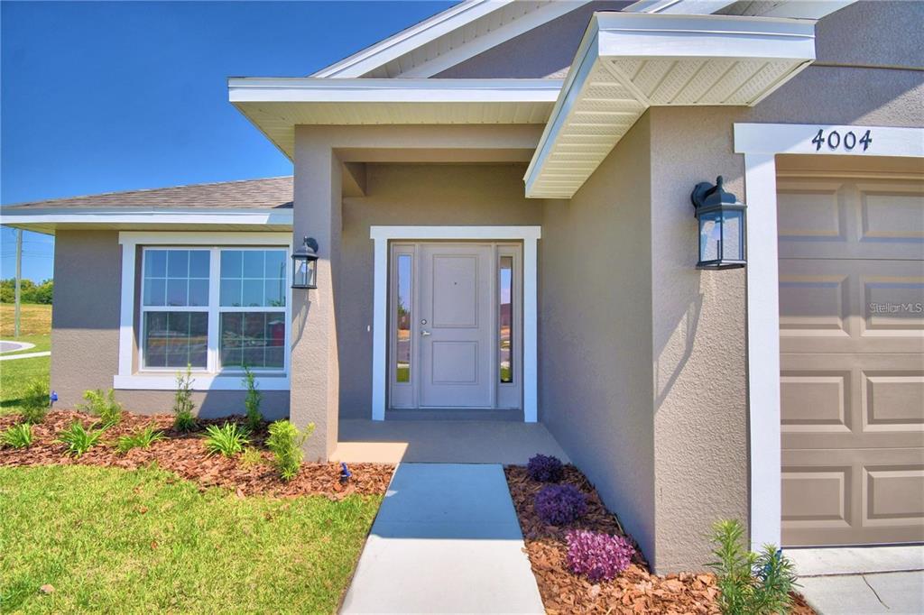 A beige house exterior features a front door with sidelights, a garage, and landscaped mulch beds — 3632 LINDBERGH STREET, LAKELAND, FL