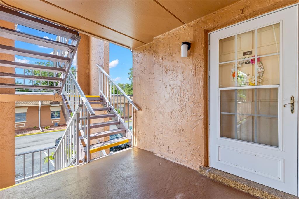 An exterior view of an apartment balcony with a staircase and a white front door — 12760 INDIAN ROCKS ROAD UNIT 107, LARGO, FL