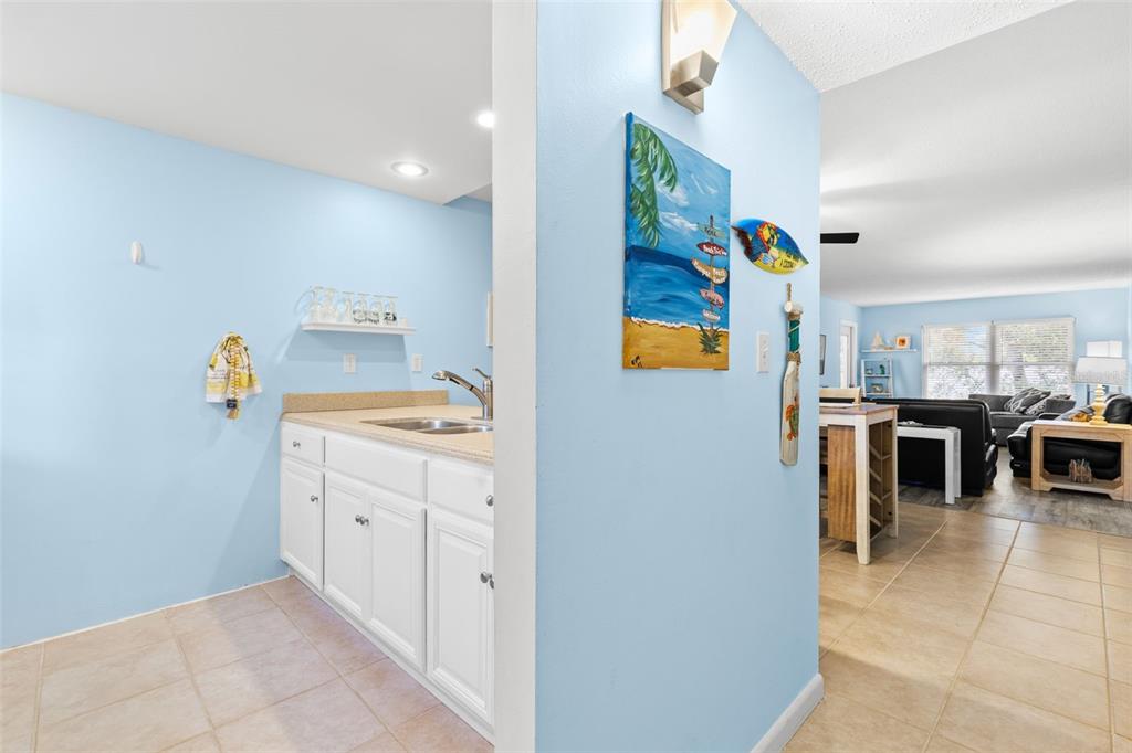 A wet bar with white cabinets and a beige countertop sits beside a living area — 12760 INDIAN ROCKS ROAD UNIT 107, LARGO, FL