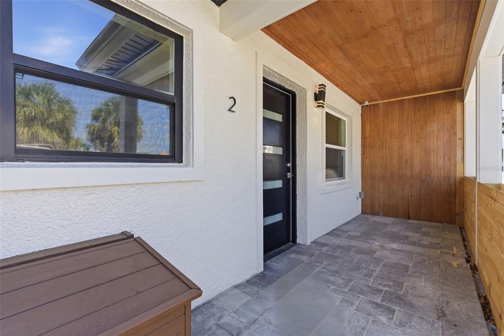 A modern front entryway features a black door, wood-paneled ceiling, and stone-tiled porch — 113 145TH AVENUE E UNIT 2, MADEIRA BEACH, FL