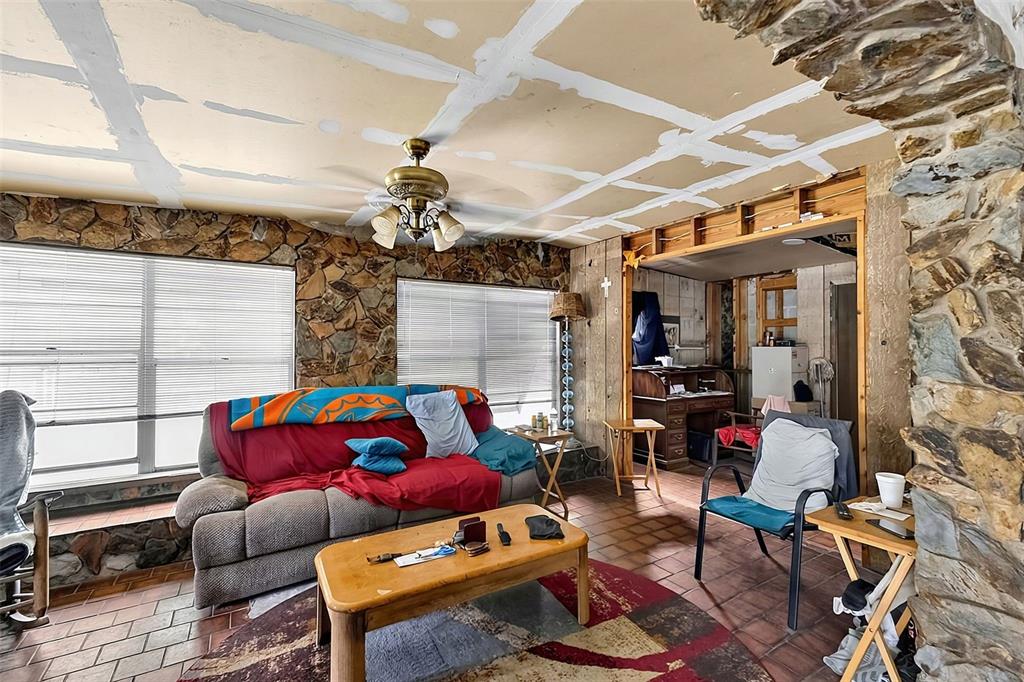 A living room features stone walls, a tiled floor, and an unfinished drywall ceiling — 28070 SUNSET DRIVE, PUNTA GORDA, FL