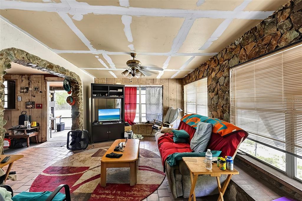 A living room features a stone accent wall, tile flooring, and an unfinished ceiling — 28070 SUNSET DRIVE, PUNTA GORDA, FL