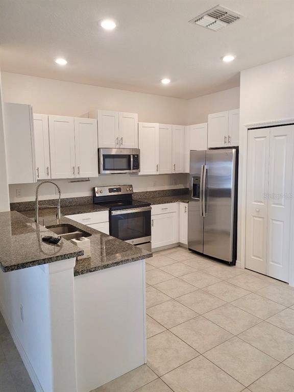 A kitchen features white cabinets, granite countertops, stainless steel appliances, and light-colored tile flooring — 5122 FORUM BOULEVARD, HOLIDAY, FL