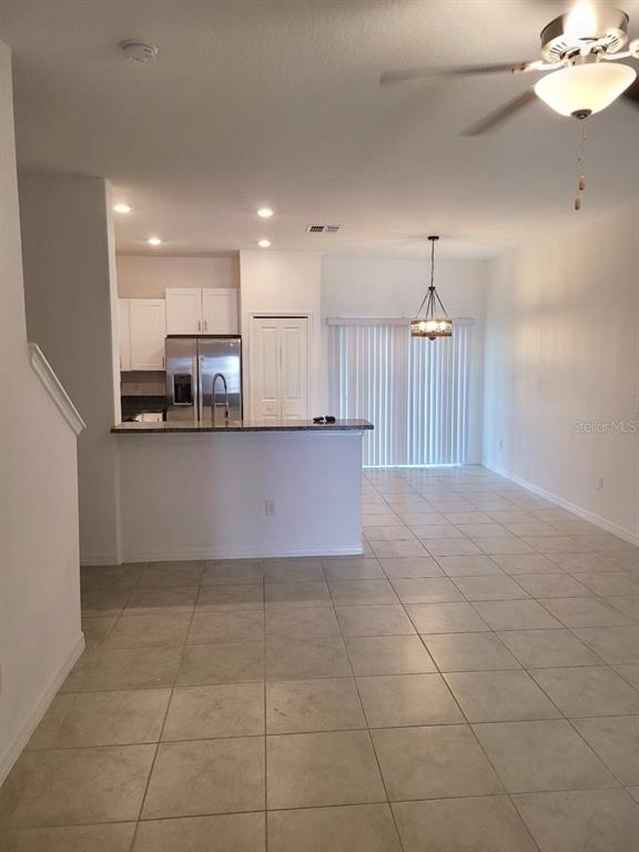 An open-concept kitchen with a breakfast bar overlooks a tiled living area with sliding doors — 5122 FORUM BOULEVARD, HOLIDAY, FL