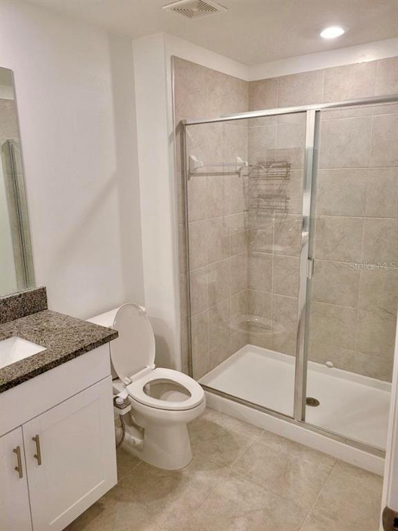 A bathroom features a white vanity with a granite countertop, a toilet, and a tiled shower — 5122 FORUM BOULEVARD, HOLIDAY, FL
