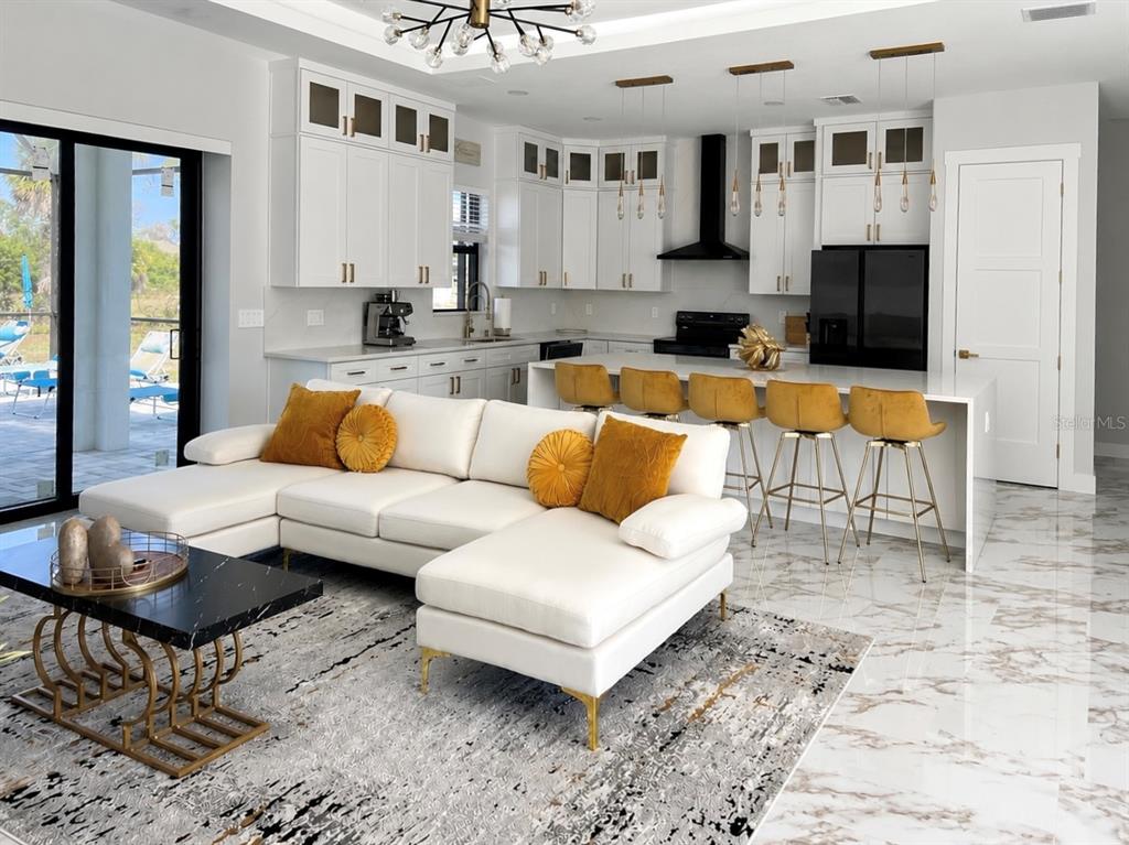 An open-concept kitchen and living area features white cabinetry, gold accents, and marble-look flooring — 61 TEE VIEW TERRACE, ROTONDA WEST, FL
