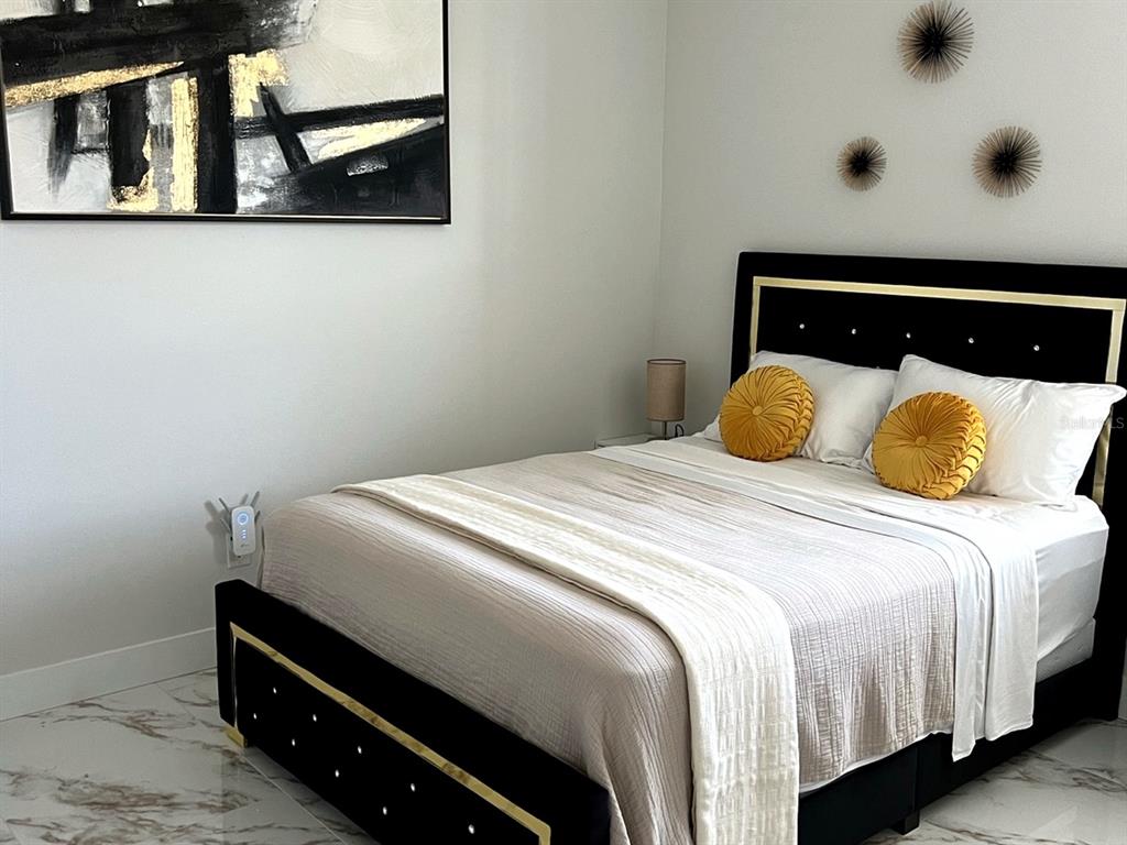 A bedroom features a black and gold bed frame, white bedding, and abstract wall art — 61 TEE VIEW TERRACE, ROTONDA WEST, FL