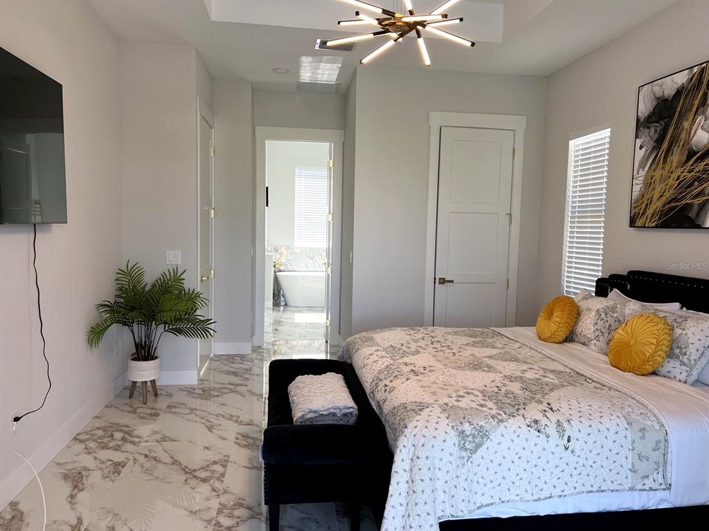 A bedroom features marble-look tile flooring, a modern chandelier, and an attached bathroom with a tub — 61 TEE VIEW TERRACE, ROTONDA WEST, FL