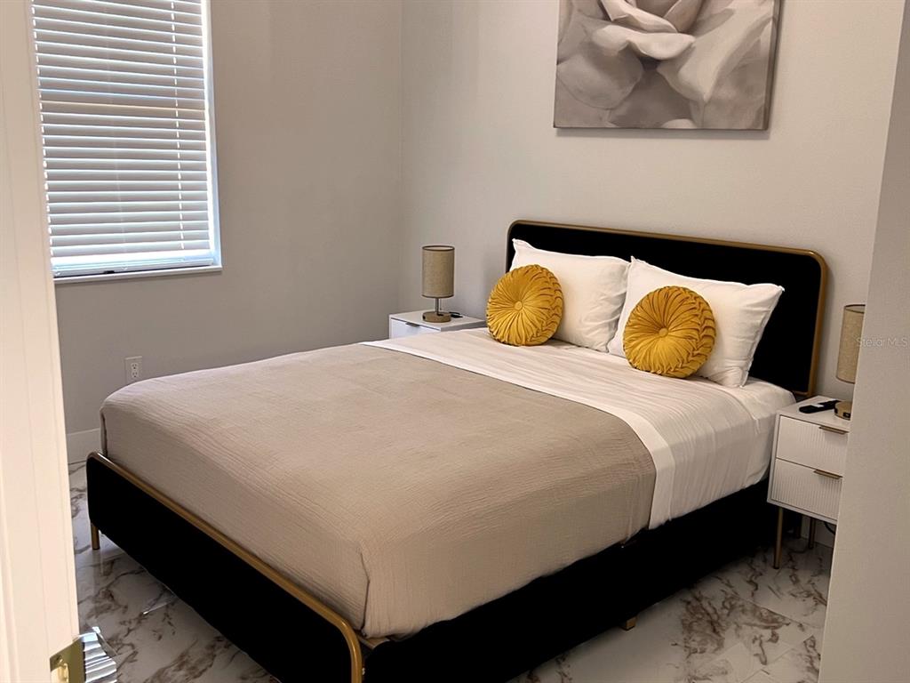 A bedroom features a bed with a black frame, yellow pillows, and marble-patterned flooring — 61 TEE VIEW TERRACE, ROTONDA WEST, FL
